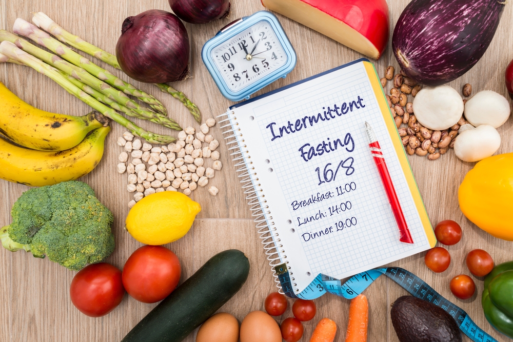 Healthy food around a clock and a notebook with a 16-8 intermittent fasting meal schedule. Concept of intermittent fasting, a diet with benefits such as the regeneration mechanism of autophagy.