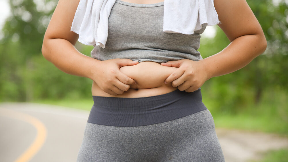 Women in park wearing workout athleisure grabbing her belly showing belly fat