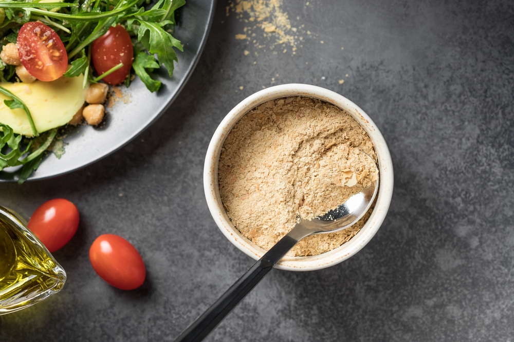 Nutritional yeast flakes in ceramic bowl on dark background. Dietary supplement, superfood. top view