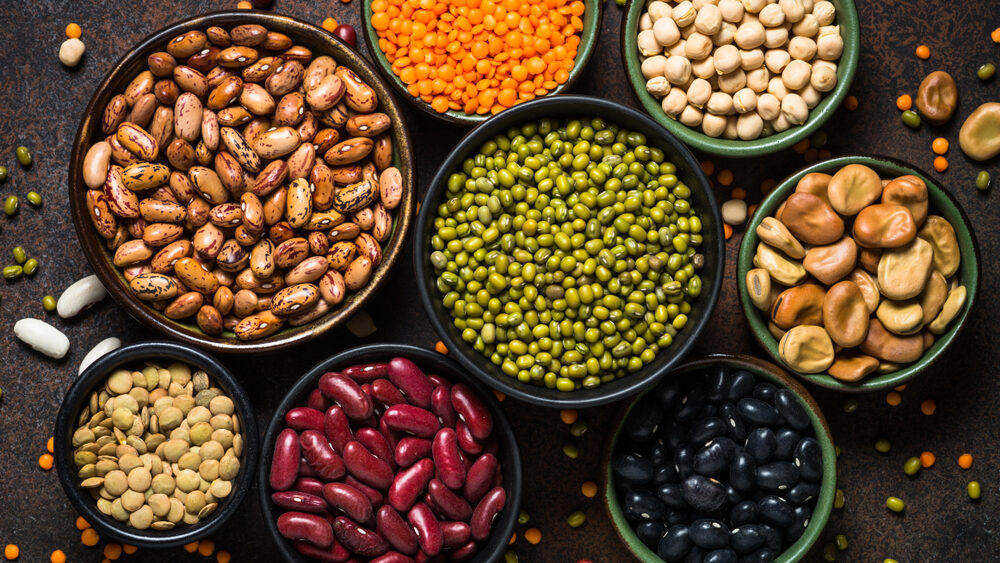 Legumes, lentils, chikpea and beans assortment in different bowls on stone table. Top view.
