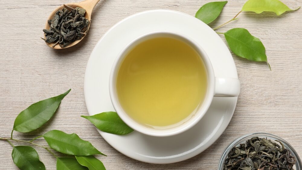 Refreshing green tea in cup, spoon and leaves on wooden table, flat lay
